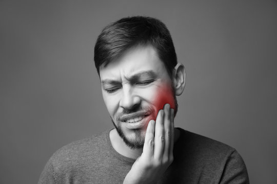 Handsome man suffering from toothache on grey background