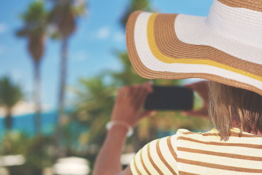 Young woman in sunhat making photo of amazing sea view with her smartphone. Santa Susanna. Cataluna. Spain.