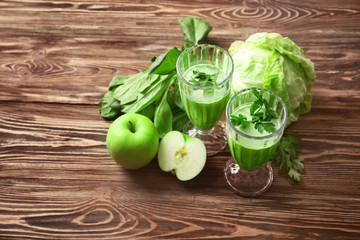 Glasses of green healthy juice with ingredients on wooden table