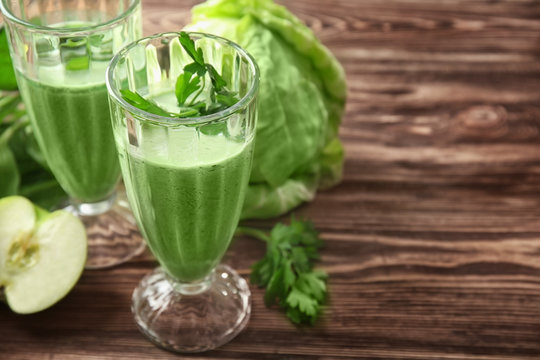 Glasses of green healthy juice with ingredients on wooden table