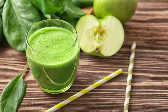 Glass of green healthy juice with ingredients on wooden table