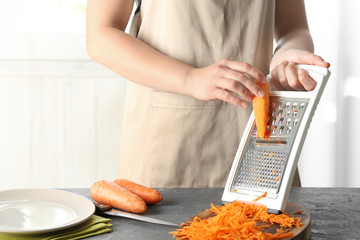Woman grating carrot on kitchen table