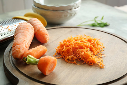 Wooden board with heap of grated carrot on kitchen table