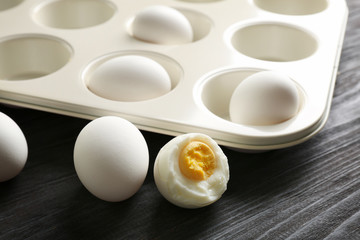 Muffin tin and hard boiled eggs on wooden table