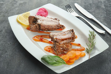 Plate with delicious ribs and vegetables on table