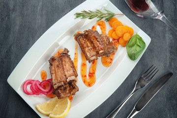 Plate with delicious ribs and vegetables on table