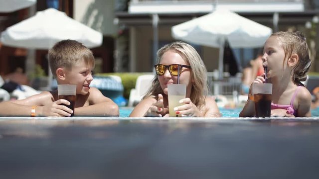 Family mother and son and daughter in the summer drinks cocktail in the pool