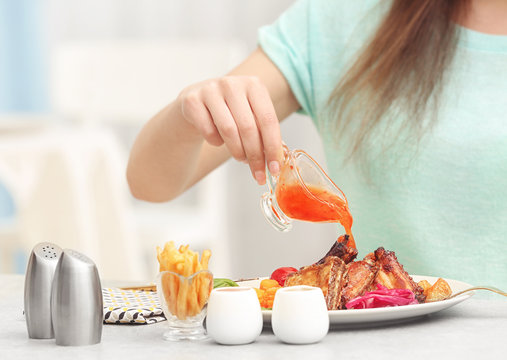 Young woman pouring sauce in plate with delicious ribs