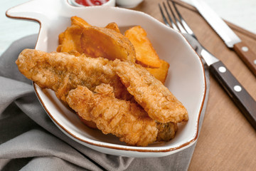 Plate with fried fish and chips on wooden board