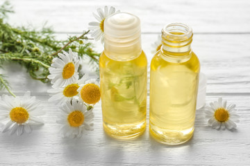 Bottles of essential oil with fresh chamomiles on table