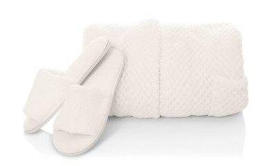 Folded bathrobe and bathing slippers on white background