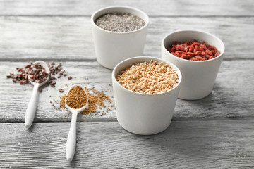 Composition with assortment of superfood products in bowls and spoons on light wooden background