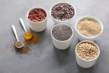 Composition with assortment of superfood products in bowls and spoons on grey textured background