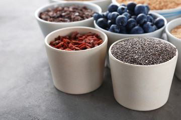 Composition with assortment of superfood products in bowls on grey textured background