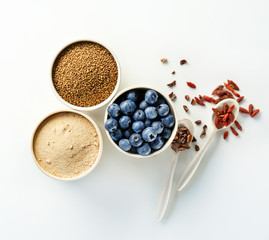 Composition with assortment of superfood products in bowls and spoons on white background, top view