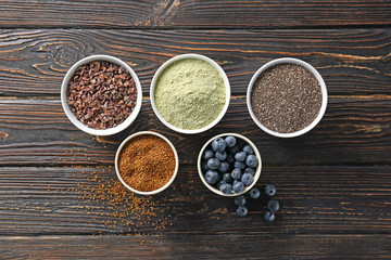Composition with assortment of superfood products in bowls on wooden background, top view