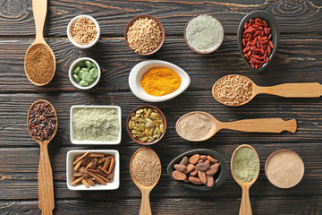 Composition with assortment of superfood products in bowls and spoons on wooden background, flat lay