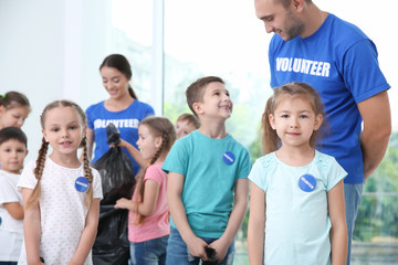 Happy volunteers and children with garbage bags indoors