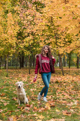 Portrait of a young woman with dog on golden autumn walk.