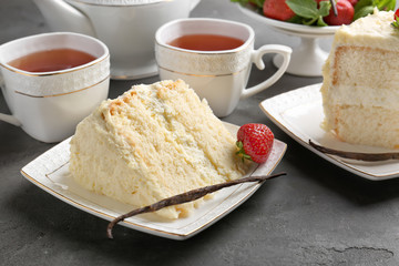 Piece of delicious vanilla cake and cups with tea on table