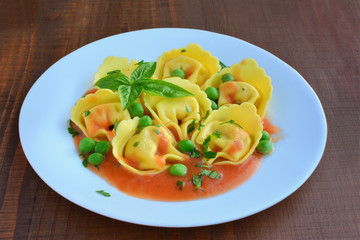 Tortelloni stuffed pasta with cheese and tomato sauce on plate over wooden table