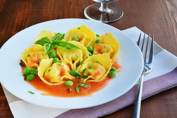 Tortelloni stuffed pasta with cheese and tomato sauce on plate over wooden table