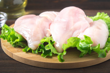 Raw chicken fillet and green salad on a round cutting board on a wooden table background. Meat ingredients for cooking.