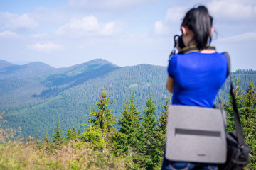 A dark-haired girl in a blue T-shirt is taking pictures of a mountain landscape. Horizontal frame