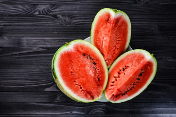 Background of three slices of a cut watermelon in a white plate on a black wooden table top view. Empty space for text