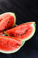 Background of three slices of a cut watermelon in a white plate on a black wooden table top view.