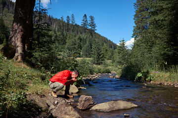 Thirsty hiker drinking water in mountain river