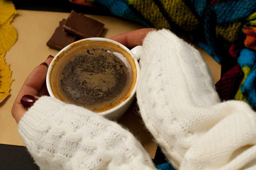 Woman's hand in a sweater holds a cup of coffee on the background of an envelope with fried leaves and colored apples, an autumnal mood