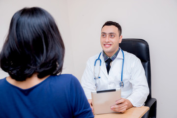 Asian man doctor holding tablet discussing with asian woman patient about examination result at table in clinic.