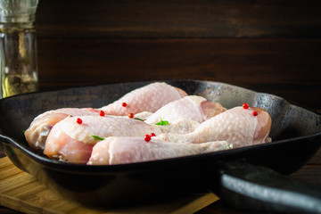 Raw chicken legs in a frying pan on a wooden table. Meat ingredients for cooking.
