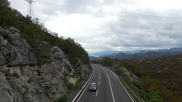 Road through the grassy hills. Footage.Mountain road. Cloudy summer day. Travel by car. Cars cross mountain road winding in twilight