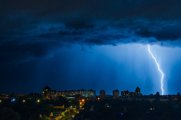 Lightning over the city in the night sky strikes the roof of the house