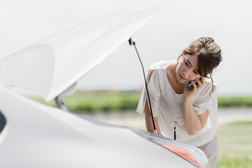 young woman checking under the hood and calling help with smart phone.