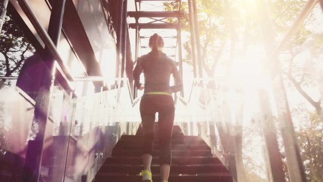 Runner Woman Jogging up Stairs, Lens Flare. 4K Steadicam STABILIZED shot. Athletic Sportswoman Running Up the Modern Sunny Glass Stairs. Healthy Lifestyle and Wellness. Achievement.  
