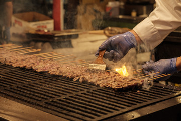 A chef brushes seasoning across meat skewers on a grill