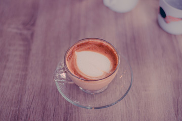 Hot coffee with heart make up on face of milk cream in glass cup on wooden table background, top view