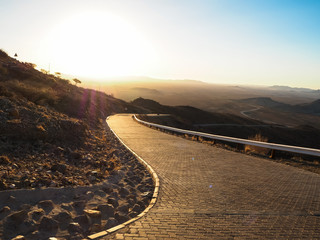Driving offroad car on adventure road trip through proper block paved curved road among dried desert and rock mountain landscape to dusty vast horizon on beautiful sunshine day © TChareon