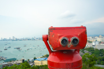 Fototapeta na wymiar Coin Operated Binocular viewer next to the waterside promenade in Pattaya (Thailand) looking out to the Bay and city. Landscape with beautiful cloudy sky, sea.