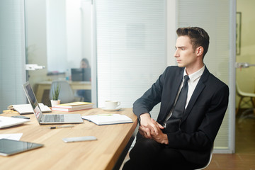 Young man in suit brainstorming by his workplace in office