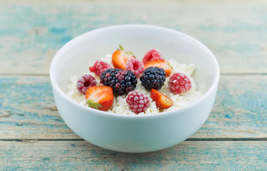 Organic cottage cheese with blackberry, strawberry and raspberry in a white ceramic bowl on the kitchen table. Dairy products for the breakfast. Healthy food concept. Top view