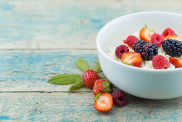 Organic cottage cheese with blackberry, strawberry and raspberry in a white ceramic bowl on the kitchen table. Dairy products for the breakfast. Healthy food concept. Top view