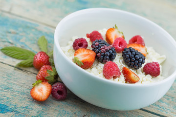 Organic cottage cheese with blackberry, strawberry and raspberry in a white ceramic bowl on the kitchen table. Dairy products for the breakfast. Healthy food concept. Top view