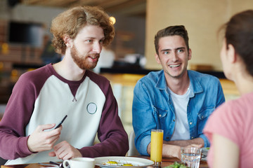 Happy guys talking to their groupmate by lunch between classes in college cafe