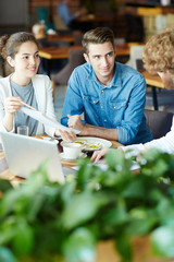 Young employees looking at their colleague during conversation in cafe