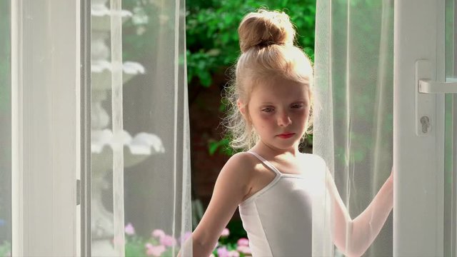 The little girl the ballerina is by the window. The lovely girl in a white tutu is by the window of a ballet school