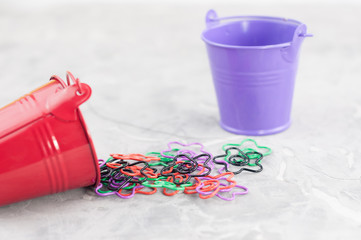 Many colored paper clips in form of star poured out of red metal bucket and one empty bucket on old gray cement